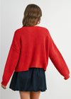 Person wearing a red sweater and navy skirt on a plain background