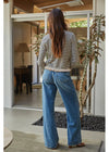 A woman viewed from behind wearing a black and white striped long-sleeve top with a ruffled hem and wide-leg blue denim jeans, standing in a modern home entryway.