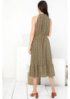 A woman viewed from behind wearing a sleeveless midi dress with a brown, black, and beige geometric pattern. She is standing in a bright, minimalist room with white walls and light wood floors.