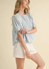 Woman wearing a light blue top and white shorts on a beige background