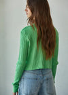 Person wearing a green knitted sweater and blue jeans against a plain background