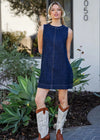 Woman wearing a blue denim dress and white cowboy boots standing outdoors.
