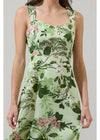 Woman wearing a sleeveless dress with floral and leaf pattern on a plain background