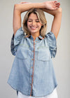Woman wearing a light blue denim shirt with rolled-up sleeves on a gray background