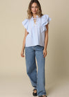 Woman wearing a light blue ruffled blouse and jeans on a beige background