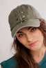 Woman wearing a green cap with floral embroidery on a plain background