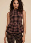 A woman modeling a sleeveless high-neck peplum top and matching pants set in a black and dark brown polka dot pattern, set against a solid beige background.