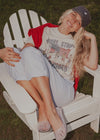 Woman sitting on a white chair outdoors wearing a graphic t-shirt and cap.