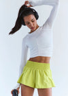 Woman in white long-sleeve top and yellow shorts holding a water bottle on a white background