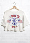White crop top with 'Surfin' The Beach Boys USA' graphic on a white brick wall background