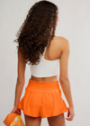 Person wearing a white crop top and orange shorts on a plain background
