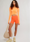 Person wearing an orange long-sleeve top and shorts with a beige bag on a light gray background