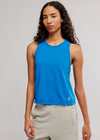 Woman wearing a blue sleeveless top and beige pants against a plain background