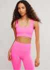 Woman wearing a bright pink sports bra and leggings on a plain background