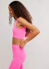 Woman wearing a pink sports bra and leggings on a light gray background