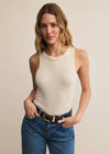 Woman wearing a white tank top and blue jeans against a beige background