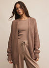Woman wearing a brown knit cardigan over a matching top and pants on a beige background