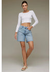 Woman wearing a white long-sleeve crop top and denim shorts on a plain background