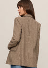 Woman wearing a brown checkered blazer and blue jeans on a beige background