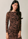 Woman wearing a brown dress with black floral patterns against a plain background
