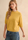 Woman wearing a yellow sweater and blue jeans against a beige background