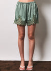 Green satin shorts with lace trim worn by a person on a plain background