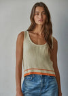 Woman wearing a beige ribbed tank top with orange trim and blue jeans against a gray background
