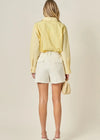 Woman wearing a yellow blouse and white shorts against a beige background