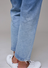 Close-up of light blue jeans and white sneakers on a neutral background