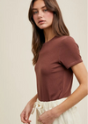 Woman wearing a brown t-shirt and white pants against a beige background