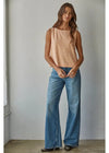 A woman modeling a sleeveless top with horizontal peach and white stripes, paired with wide-leg blue jeans, standing against a plain light gray wall.