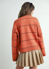 Person wearing a striped orange sweater and beige skirt on a light gray background
