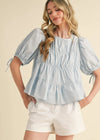 Woman wearing a light blue blouse with puff sleeves and white shorts on a beige background