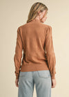 Woman wearing a brown sweater and light blue jeans against a beige background