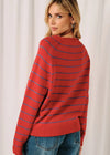 A woman wearing a red knit sweater with thin blue horizontal stripes, shown from the back and side against a soft white curtain background.