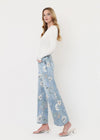 Woman wearing a white top and light blue floral jeans on a white background