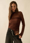 A woman modeling a brown ribbed long-sleeve mock neck top paired with dark wide-leg jeans against a plain beige background.