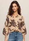Woman wearing a beige blouse with brown leaf pattern and blue jeans on a plain background