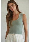 Woman wearing a light green tank top and white pants against a plain background