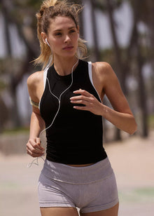  Woman running outdoors with earphones, wearing a black tank top and gray shorts.
