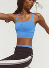 Woman wearing a blue sports bra and black leggings with white stripes against a white background