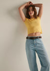 Woman wearing a yellow top and light blue jeans against a plain background
