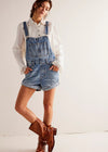 Woman wearing denim overalls and brown boots on a white background