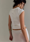 Woman wearing a white sleeveless top and skirt with gold accents against a neutral background