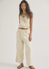 Woman wearing a white sleeveless top and cream-colored pants on a white background