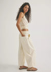 Woman wearing a white top and beige pants against a plain background