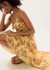 Woman wearing a yellow floral dress sitting on a white background