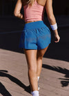 Person wearing a pink crop top and blue shorts on a wooden floor.
