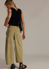 Woman wearing a black sleeveless top and beige wide-leg pants against a neutral background