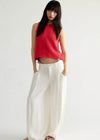 Woman wearing a red sleeveless top and white pants on a plain background